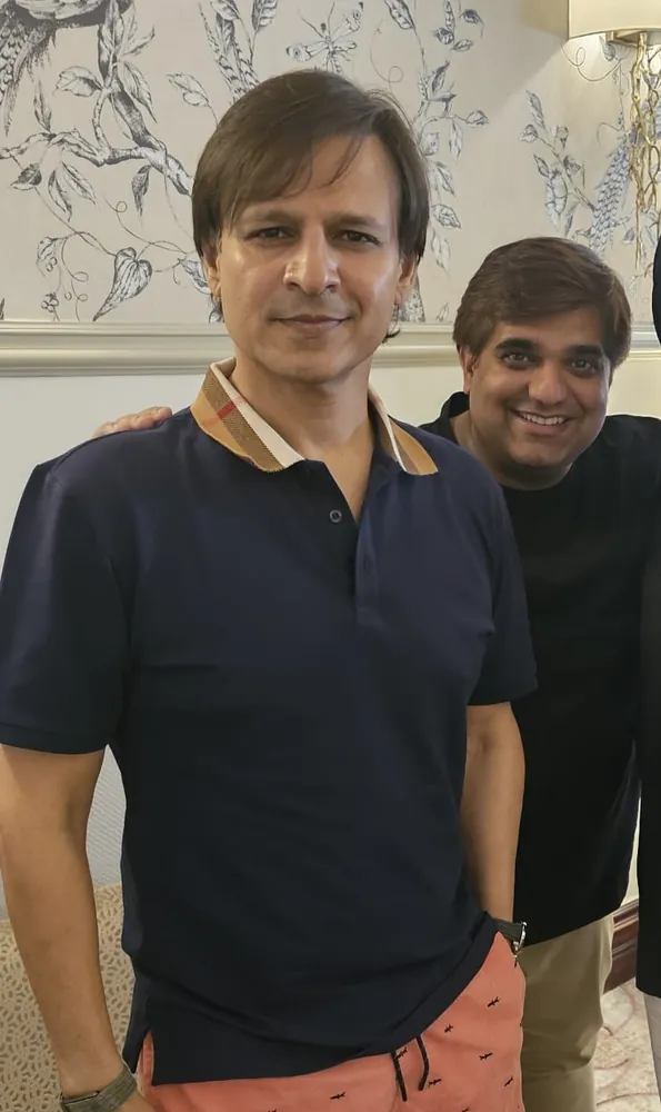 Two men posing close together: one in a navy polo shirt in front, one standing behind him