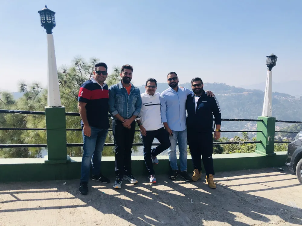 Five men standing in a row at a hillside viewpoint, with hills behind them