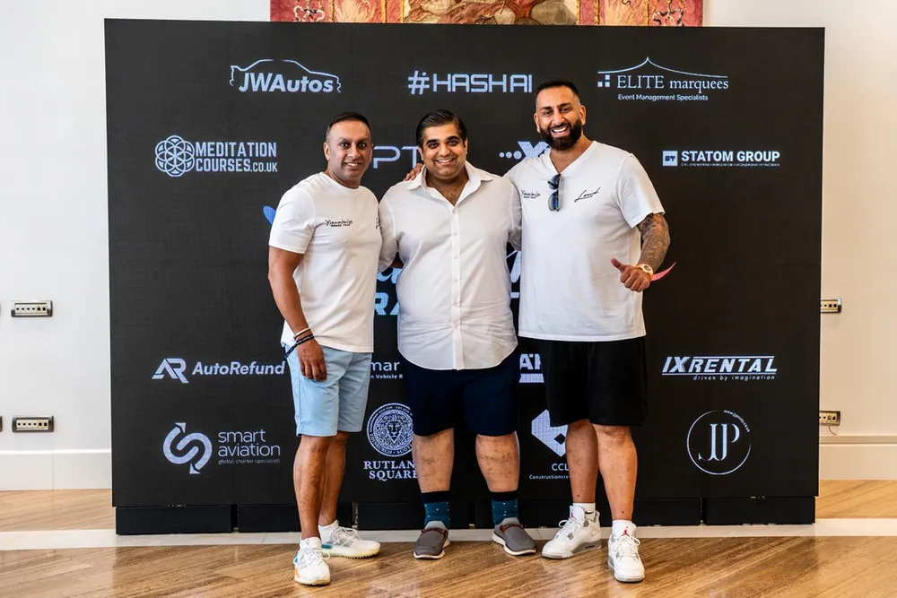 Three men standing in front of a sponsors’ wall printed with company logos, including Rutland Square