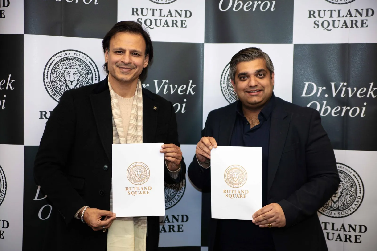 Dr Vivek Anand Oberoi and Nishant Sharma each holding a white folder printed with the Rutland Square seal