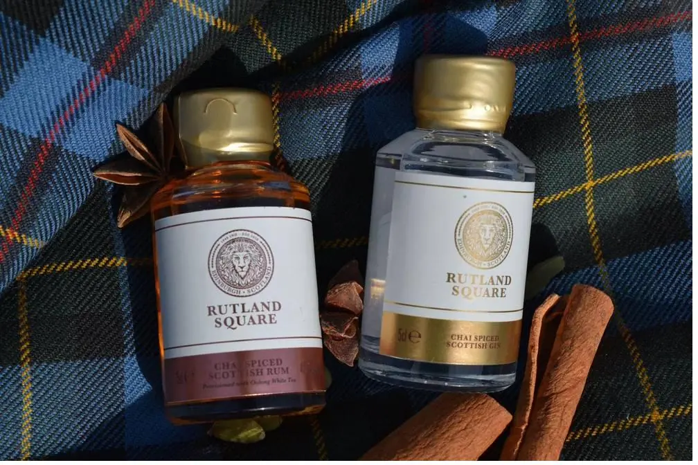 Two miniature bottles, one of rum and one of gin, on a blue tartan cloth with cinnamon sticks and star anise