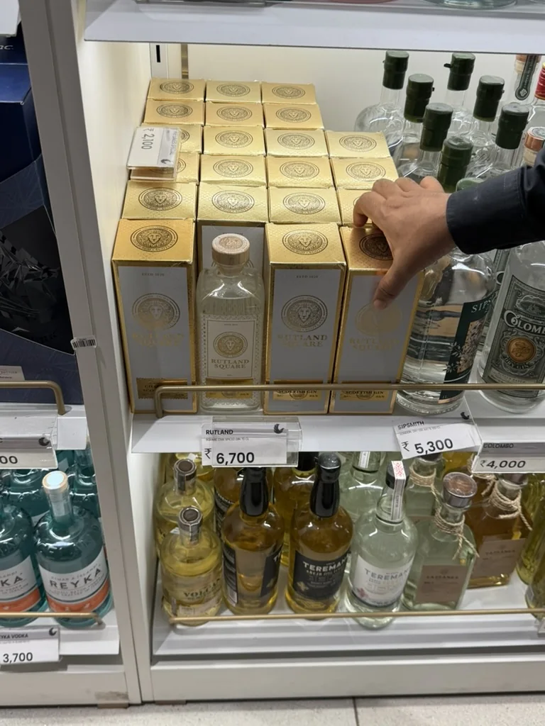Rows of gold Rutland Square gift boxes and a bottle on a duty-free shelf beside other gins, with a hand reaching for a box