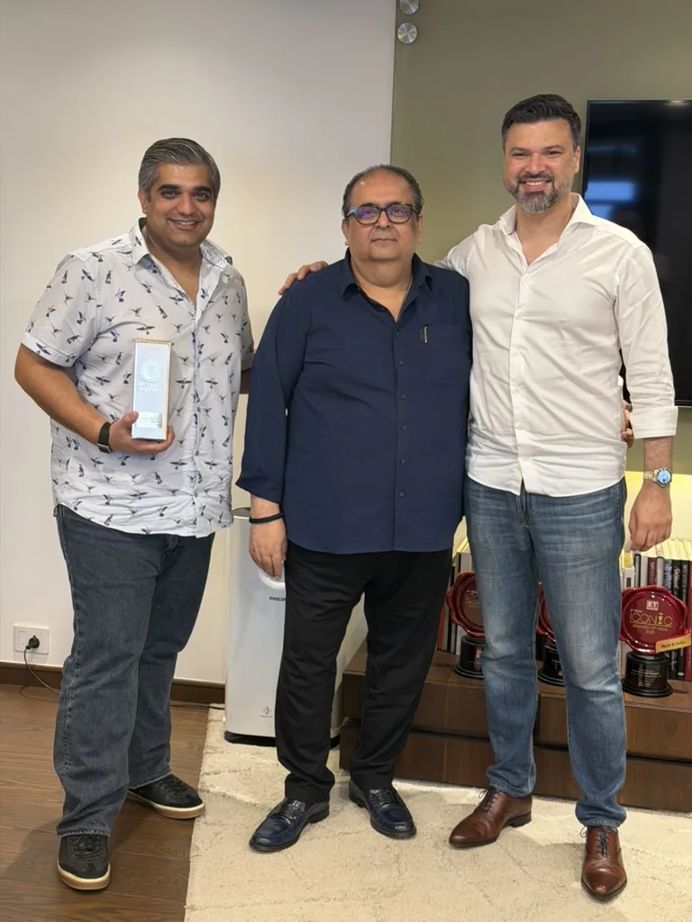 Three men standing together in an office, one holding a boxed bottle of Rutland Square, with award plaques on a shelf behind