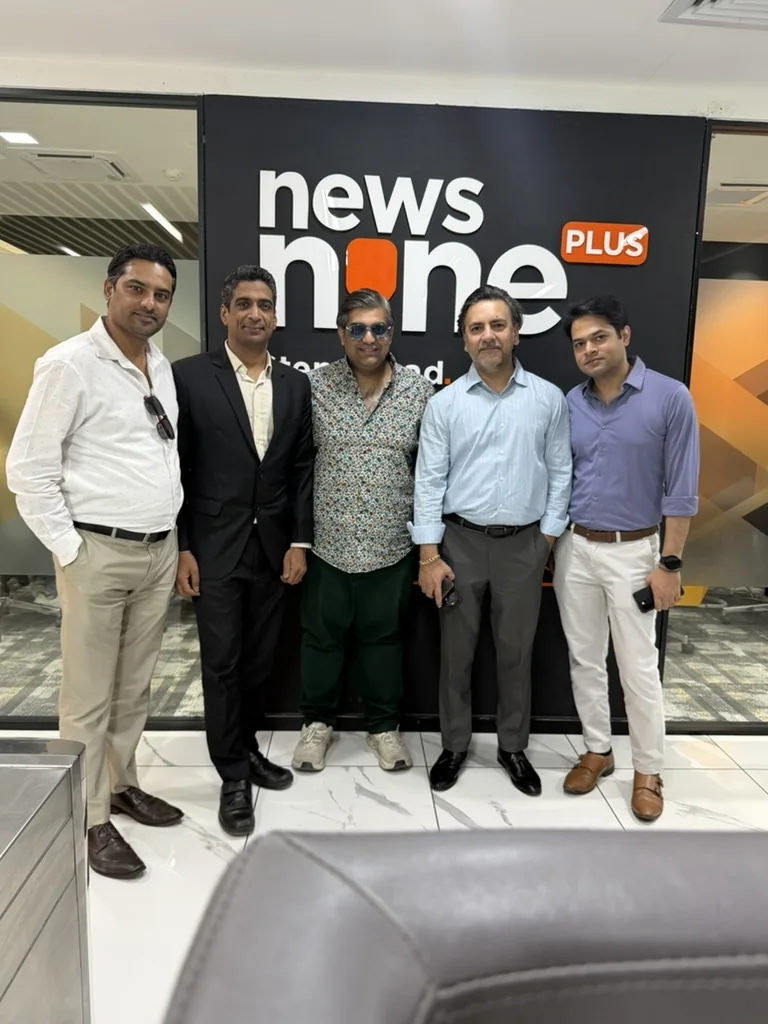 Five men standing together in front of a News Nine Plus sign in a television studio office